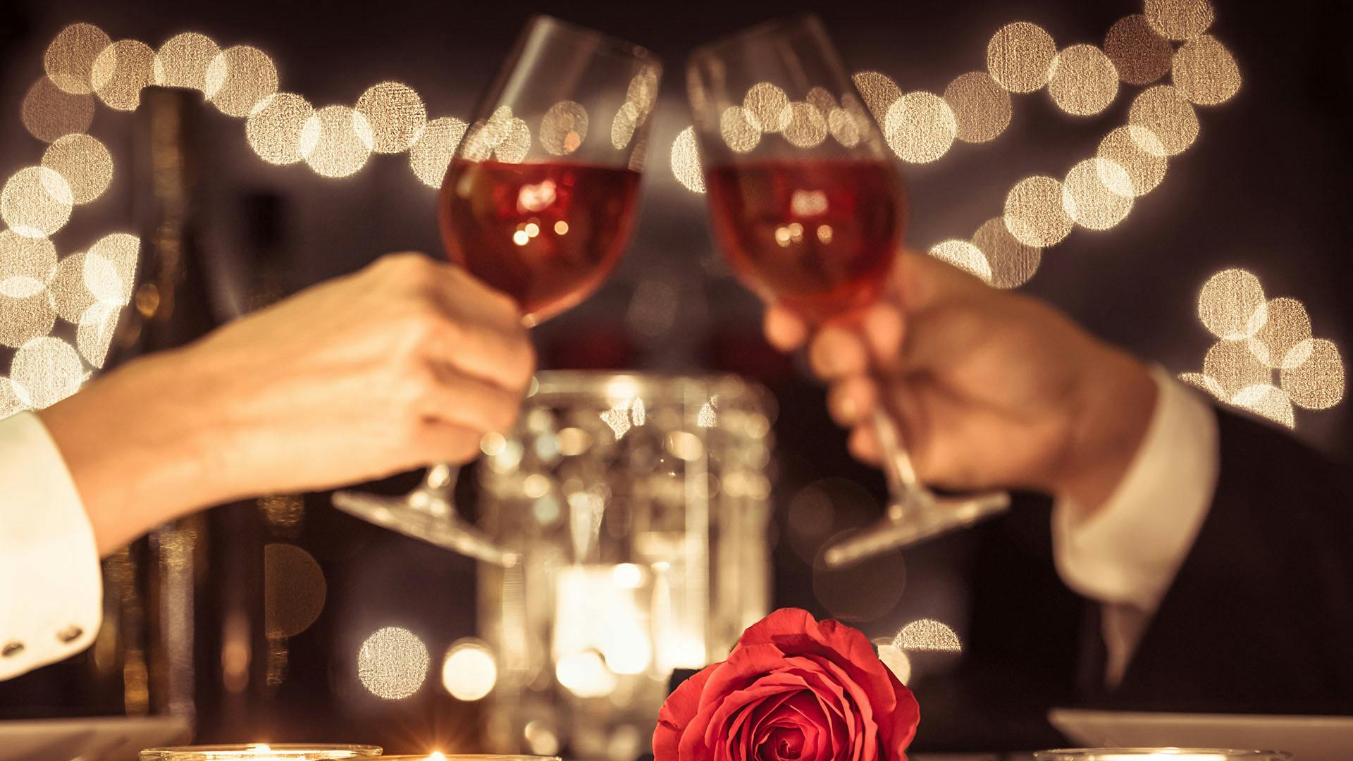 Casal em um encontro Sugar brindando durante um jantar. Velas e uma rosa em cima da mesa.