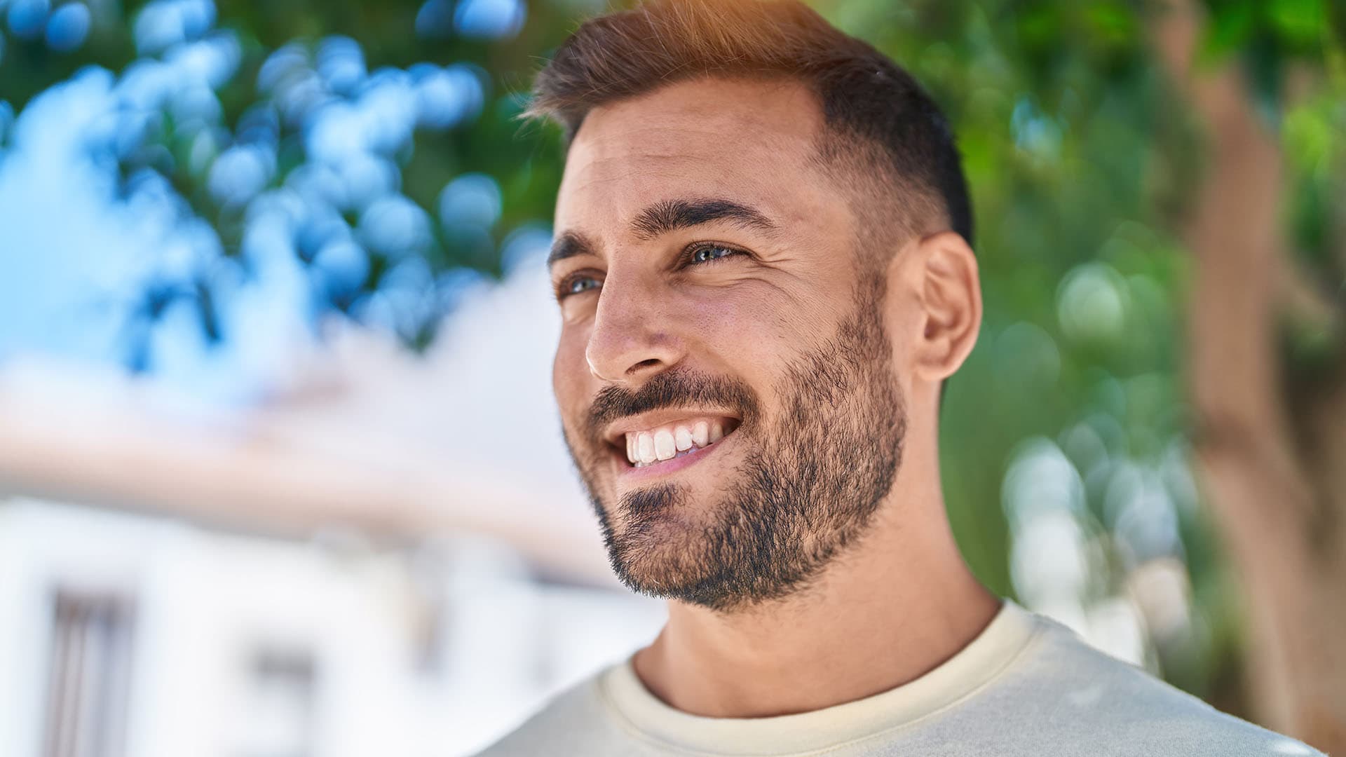 Sugar baby masculino - Homem jovem e atraente. Homem jovem de pele clara, com barba e sorrindo, caminhando na rua, representando um Sugar Baby Gay.